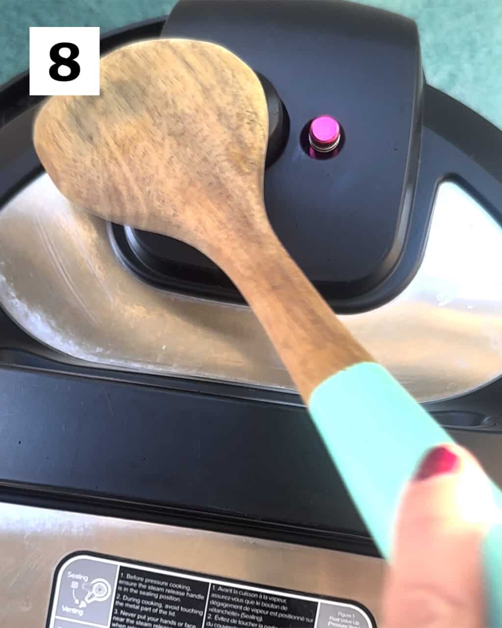 wooden spoon moving the pressure release valve over to Quick Release the Instant Pot.