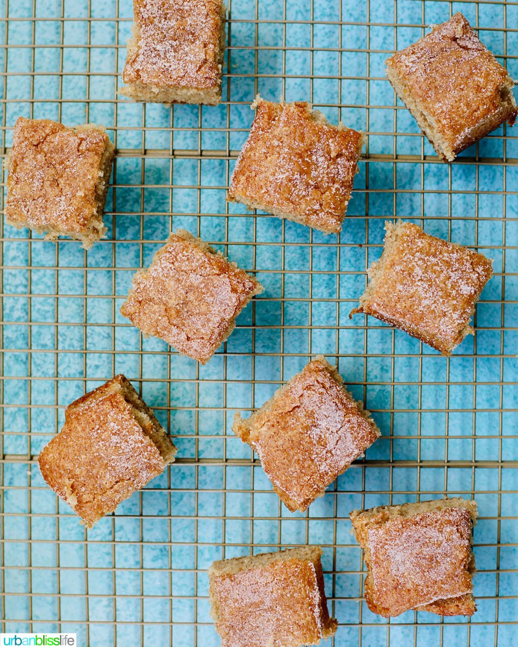 several squares of snickerdoodle snacking cakes on a cooling rack on aqua blue table.