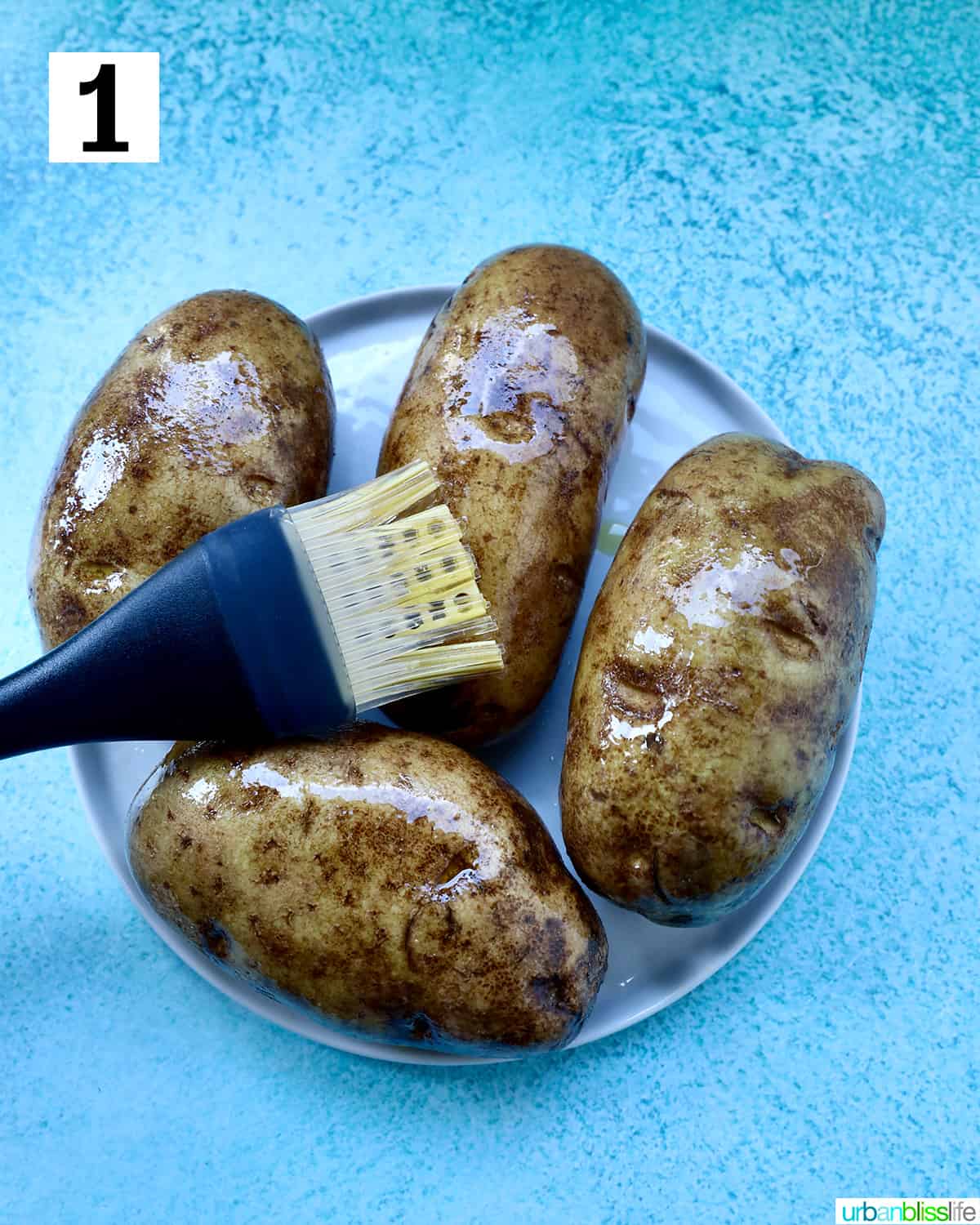 pastry brush brushing olive oil on potatoes on a plate.