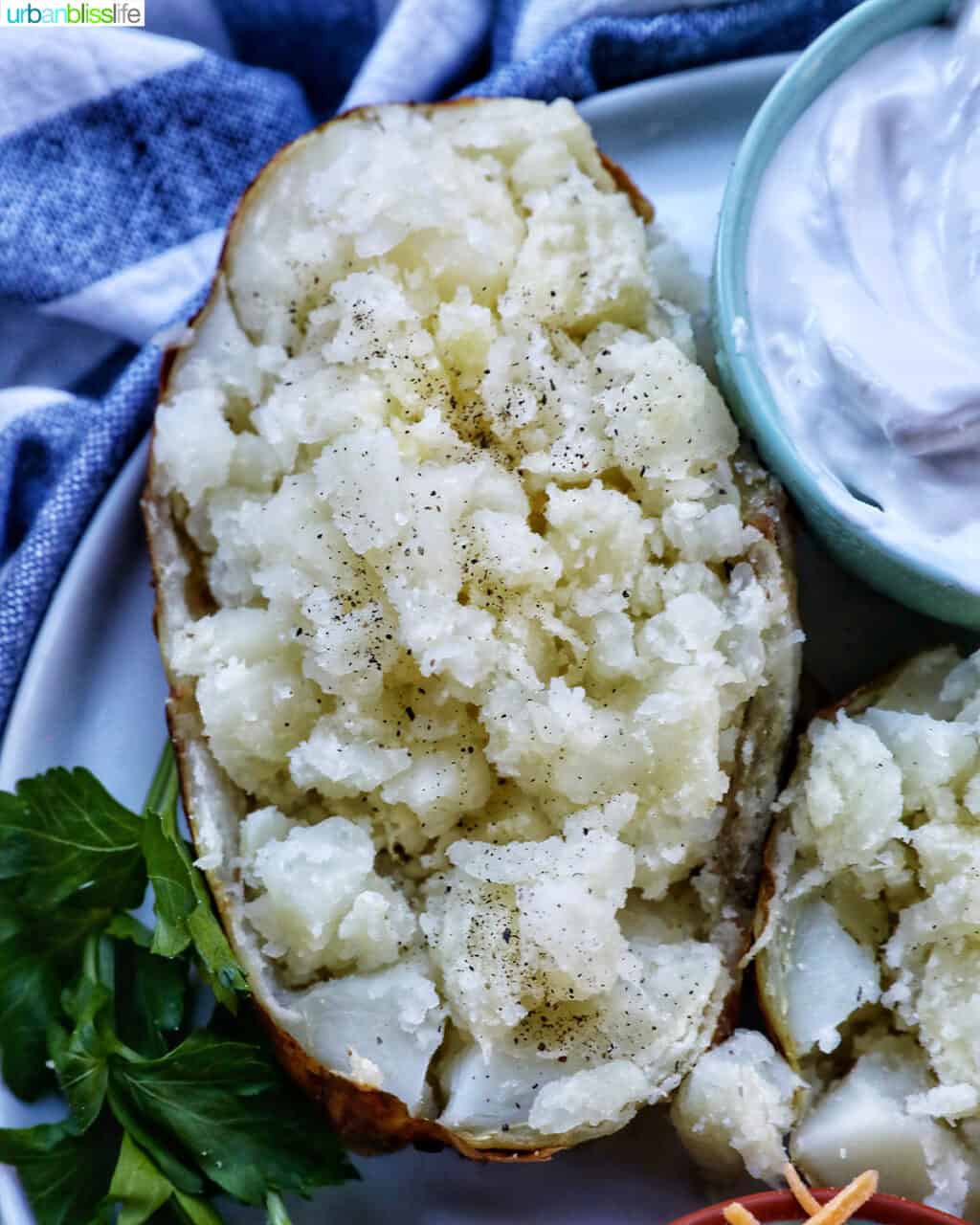 baked potato on a plate with side of sour cream and parsley.