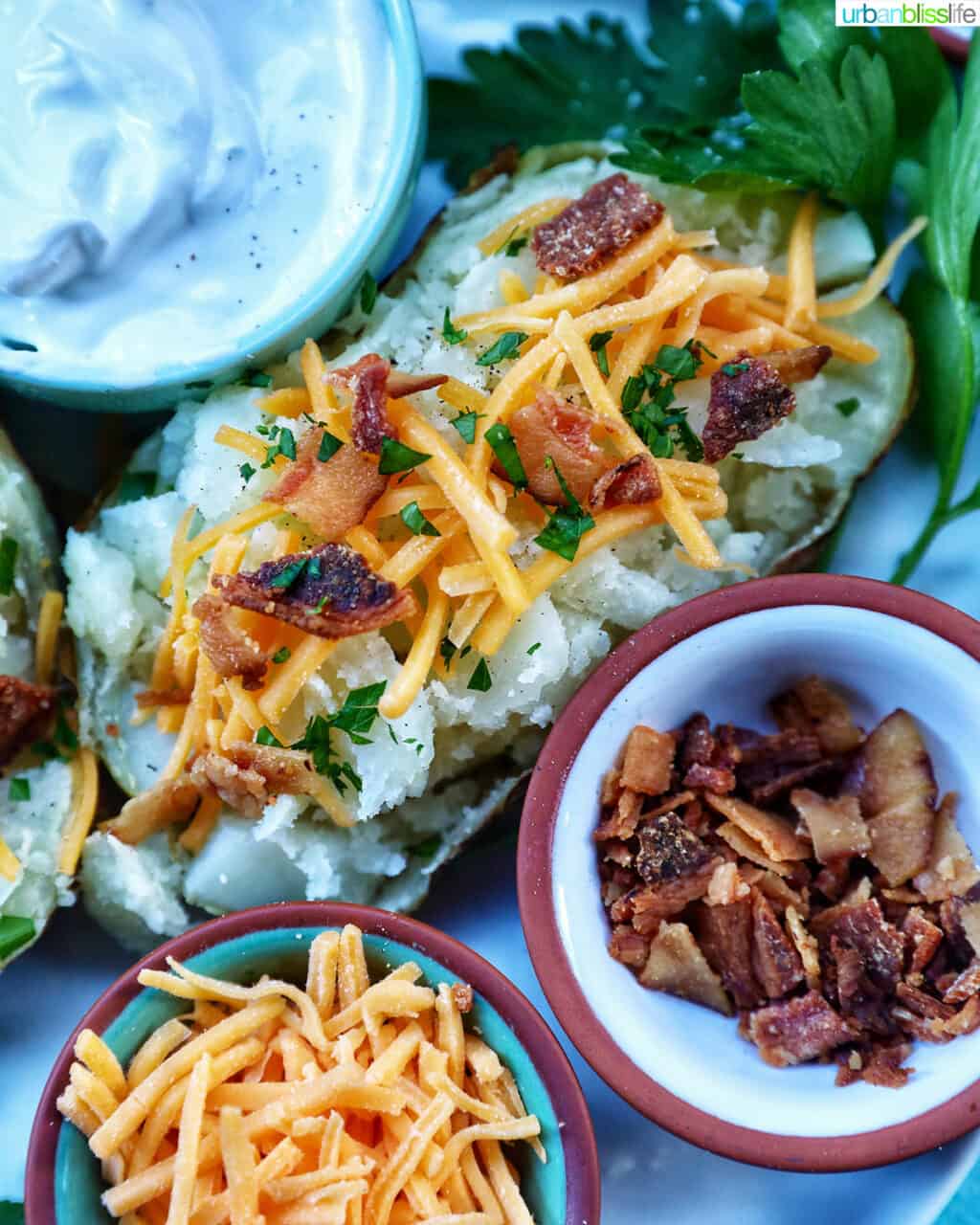Loaded air fryer baked potato with title text overlay and sides of sour cream, cheddar cheese, parsley, and bacon.