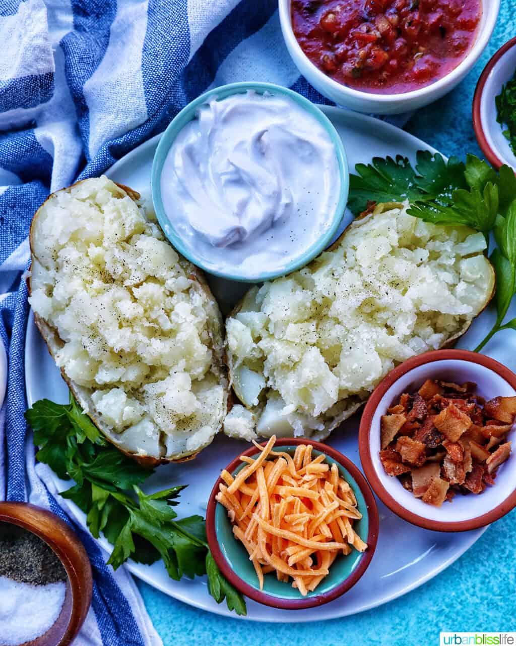 Loaded air fryer baked potato with title text overlay and sides of sour cream, cheddar cheese, parsley, and bacon.