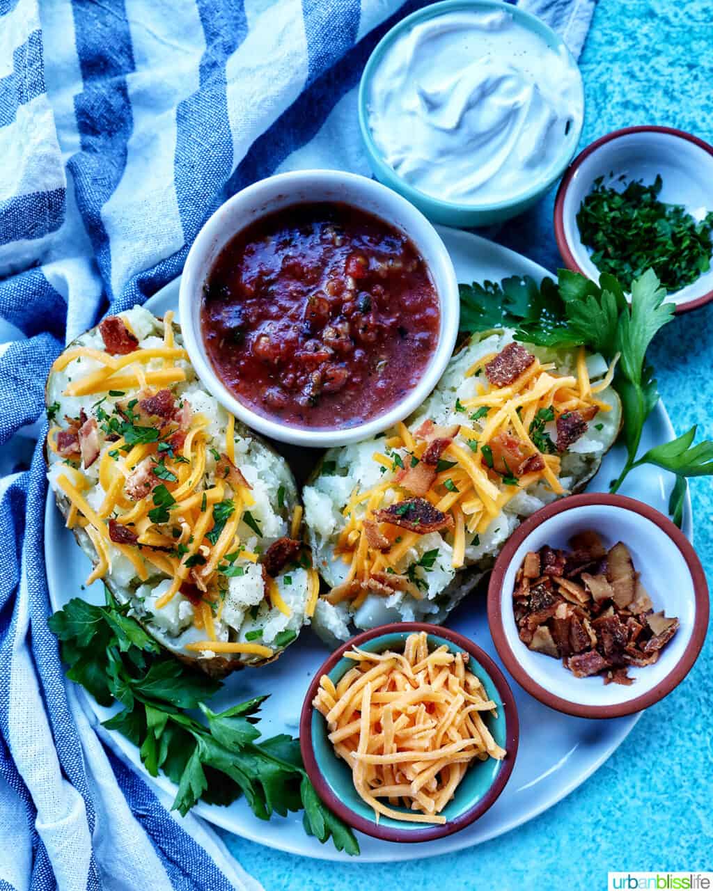 Loaded air fryer baked potato with title text overlay and sides of sour cream, cheddar cheese, parsley, and bacon.
