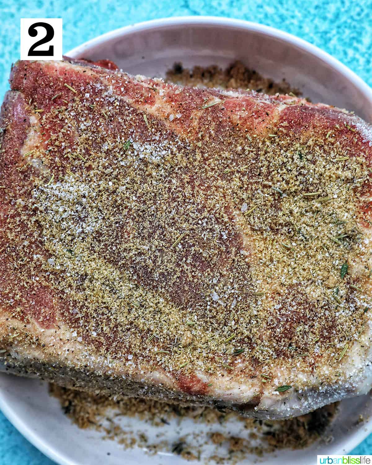 pork shoulder roast seasoned on a white plate and blue table.