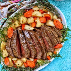Sliced sirloin tip roast surrounded by carrots, potatoes, and herbs with a side of gravy.