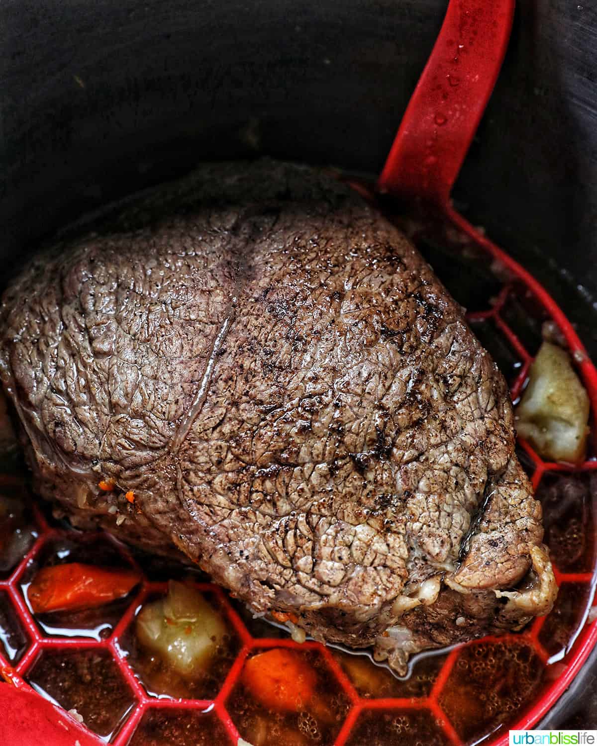 cooked sirloin tip roast in the Instant pot on a red sling with carrots and potatoes around it.
