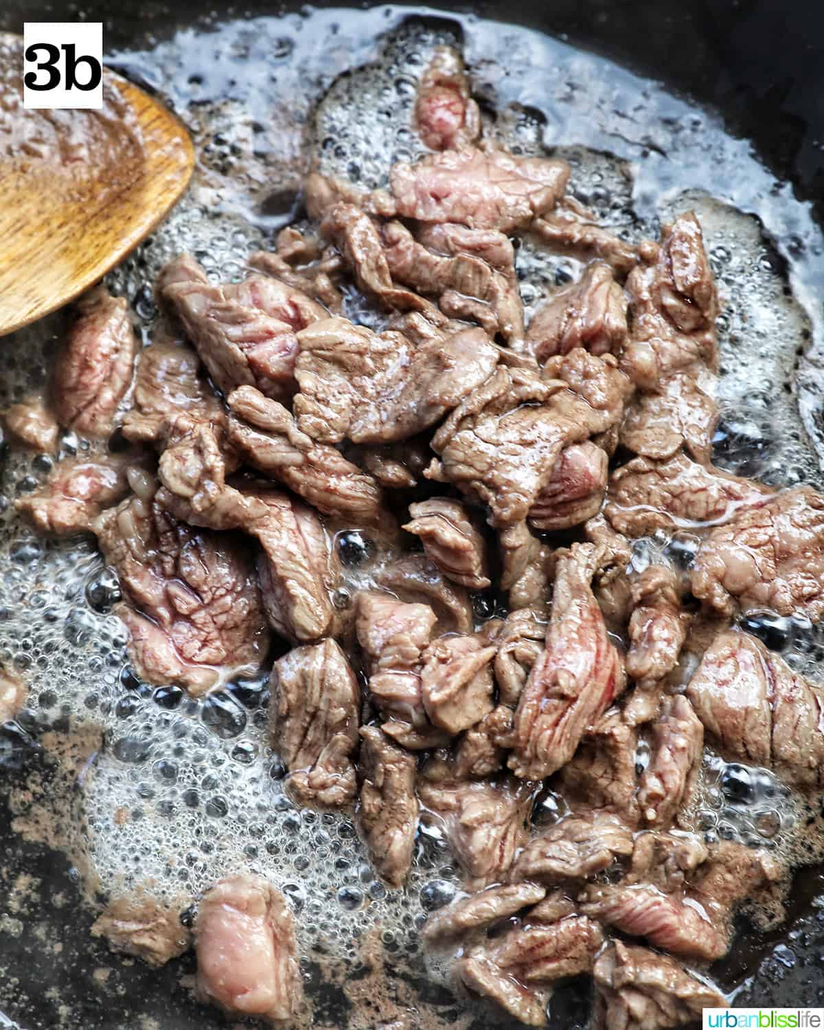 beef cooking in a wok with a wooden spoon.