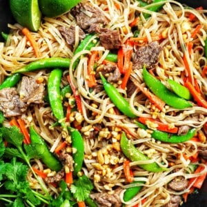 closeup of beef pad thai noodles with vegetables in a skillet with side of parsley.