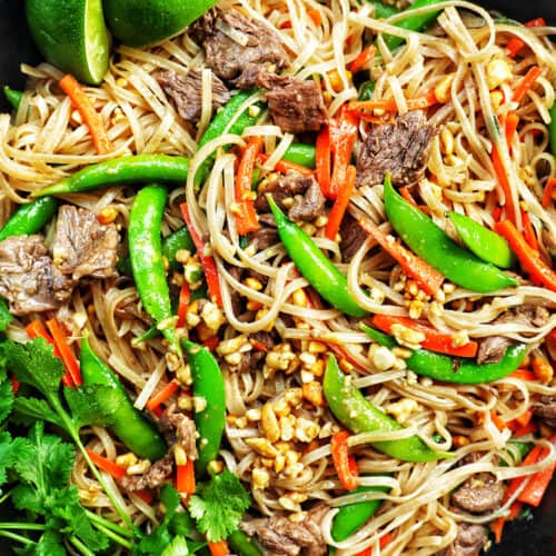 closeup of beef pad thai noodles with vegetables in a skillet with side of parsley.