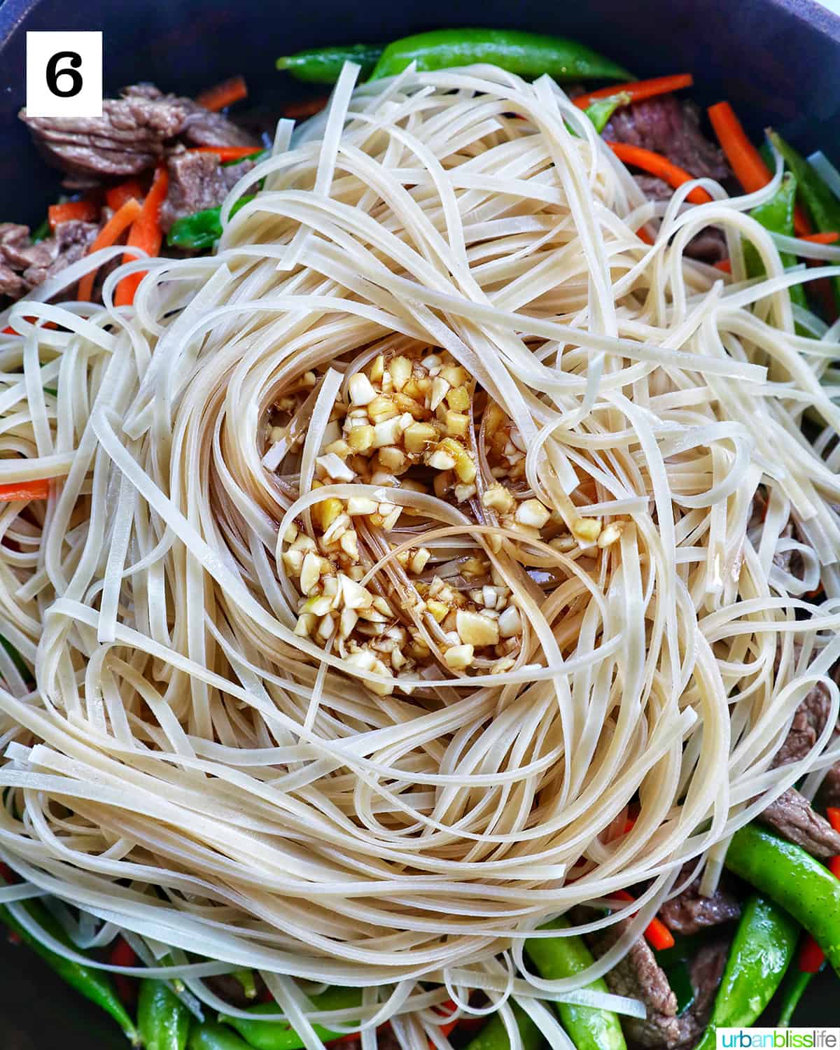 pad thai sauce on top of rice noodles on top of steak and vegetables in a pan.