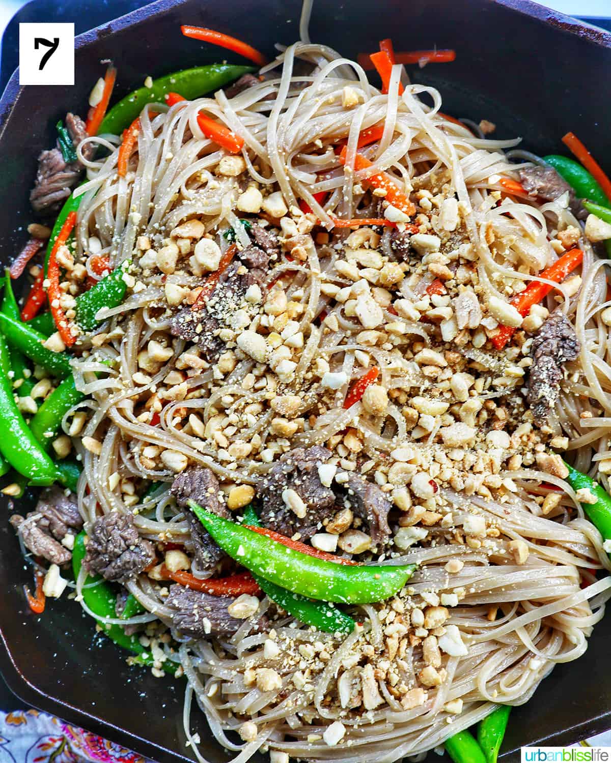 adding crushed peanuts to beef pad thai noodles with vegetables in a skillet.
