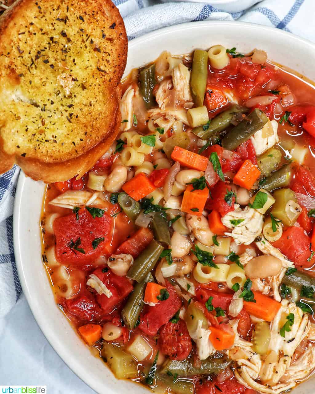 Chicken Minestrone Soup in a white bowl with side of garlic bread.