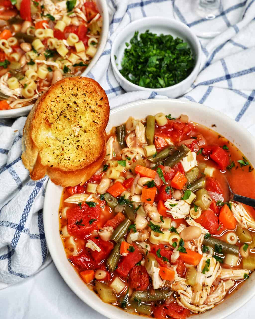 Chicken Minestrone Soup in a white bowl with side of garlic bread.