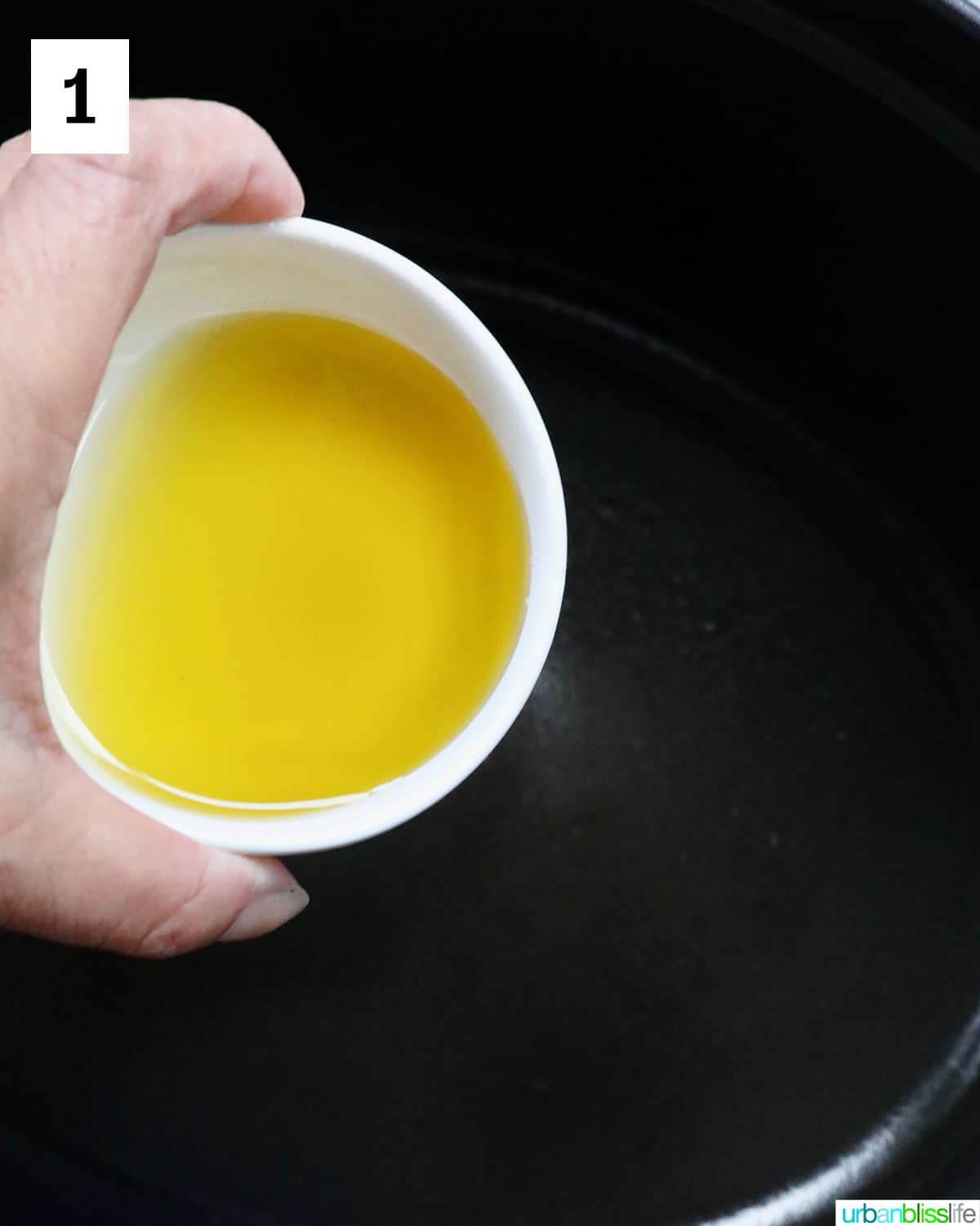 hand holding olive oil over a skillet.