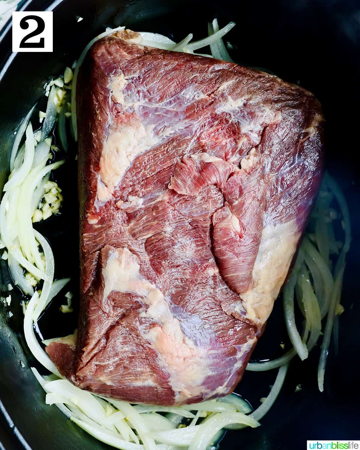 raw beef brisket with garlic and onions in a dutch oven.