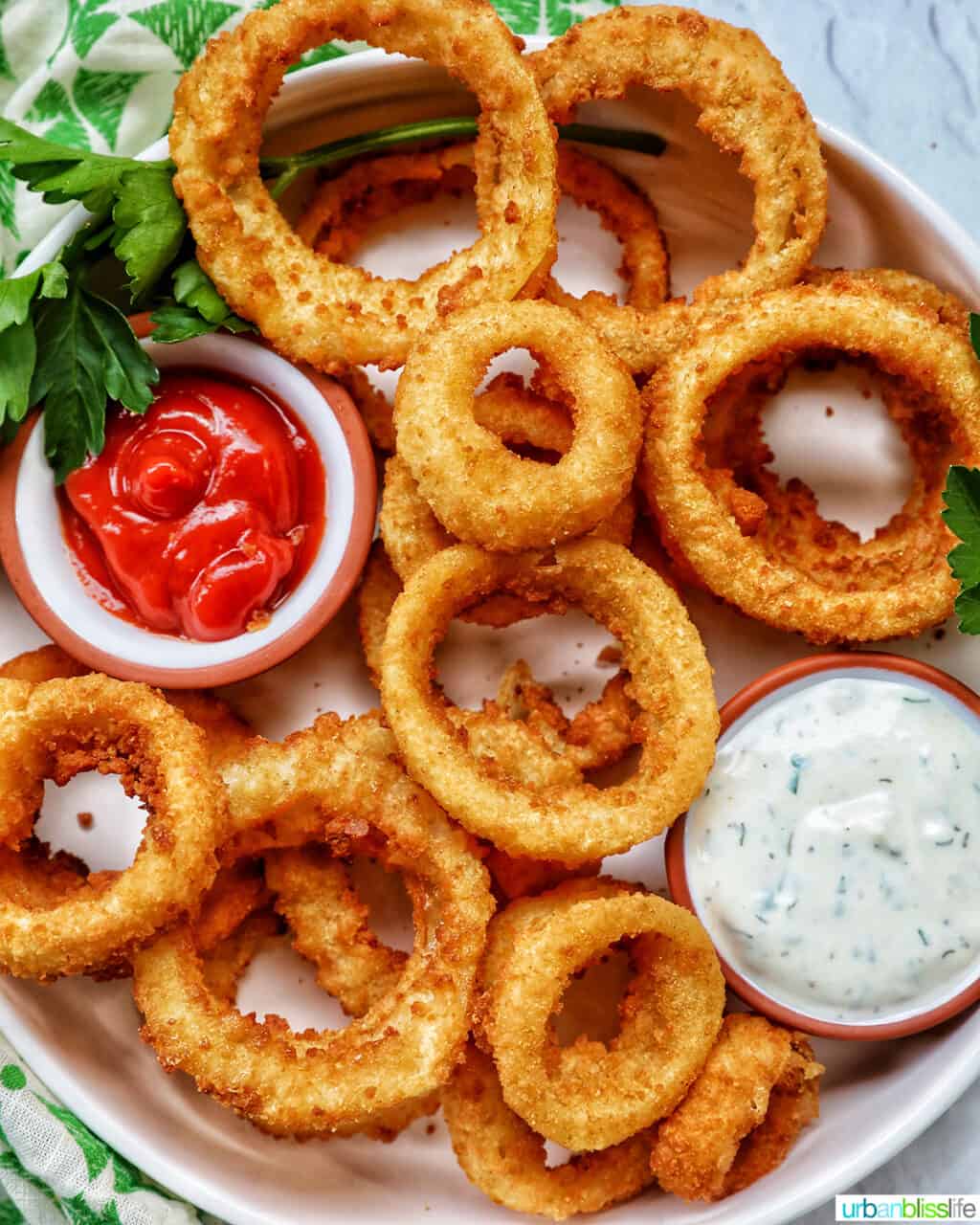 bowl of air fryer onion rings with sides of ranch dressing and ketchup..