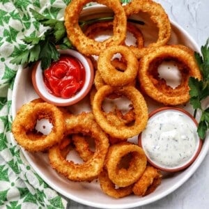 bowl of air fryer onion rings with sides of ranch dressing and ketchup..