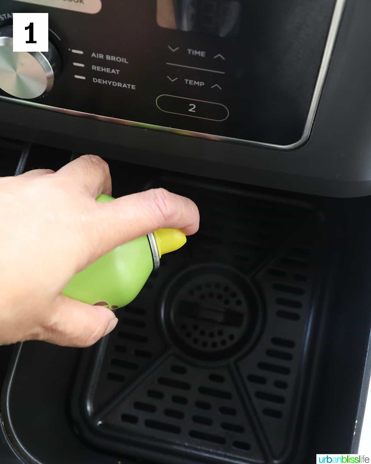 hand spraying cooking spray in air fryer basket.