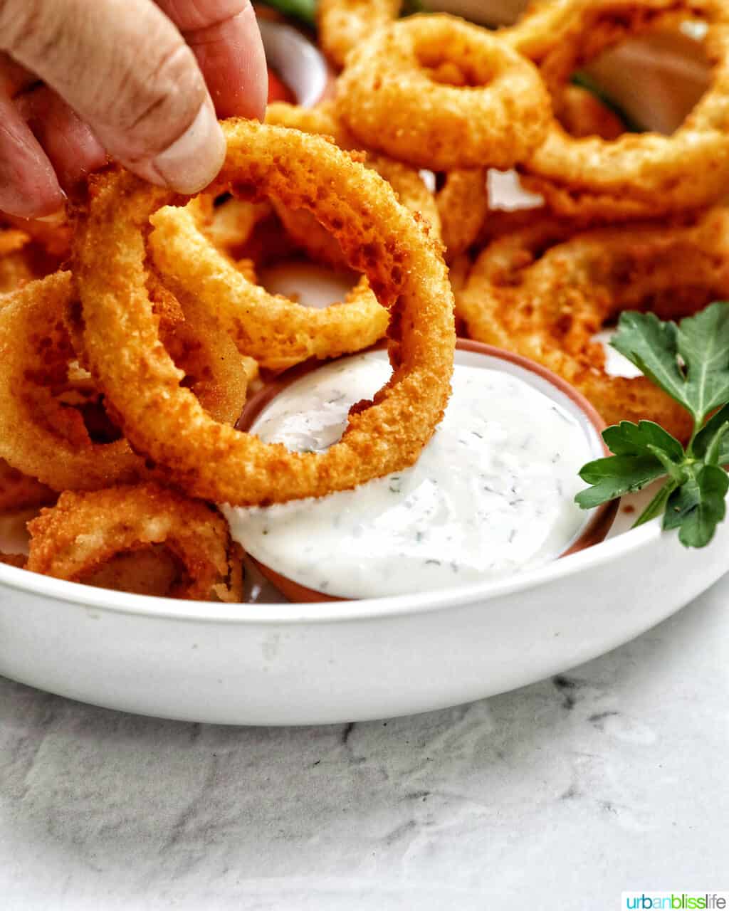 hand dipping an onion ring into a side of ranch dressing in a bowl of air fryer onion rings.