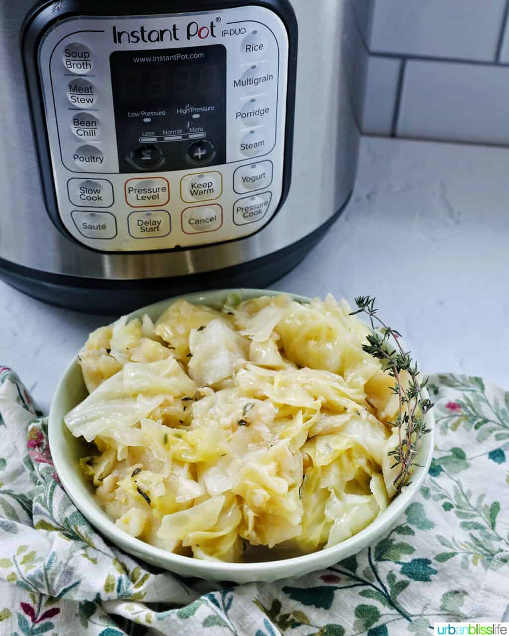 bowl of cooked instant pot cabbage with thyme sprigs in front of an Instant Pot pressure cooker.