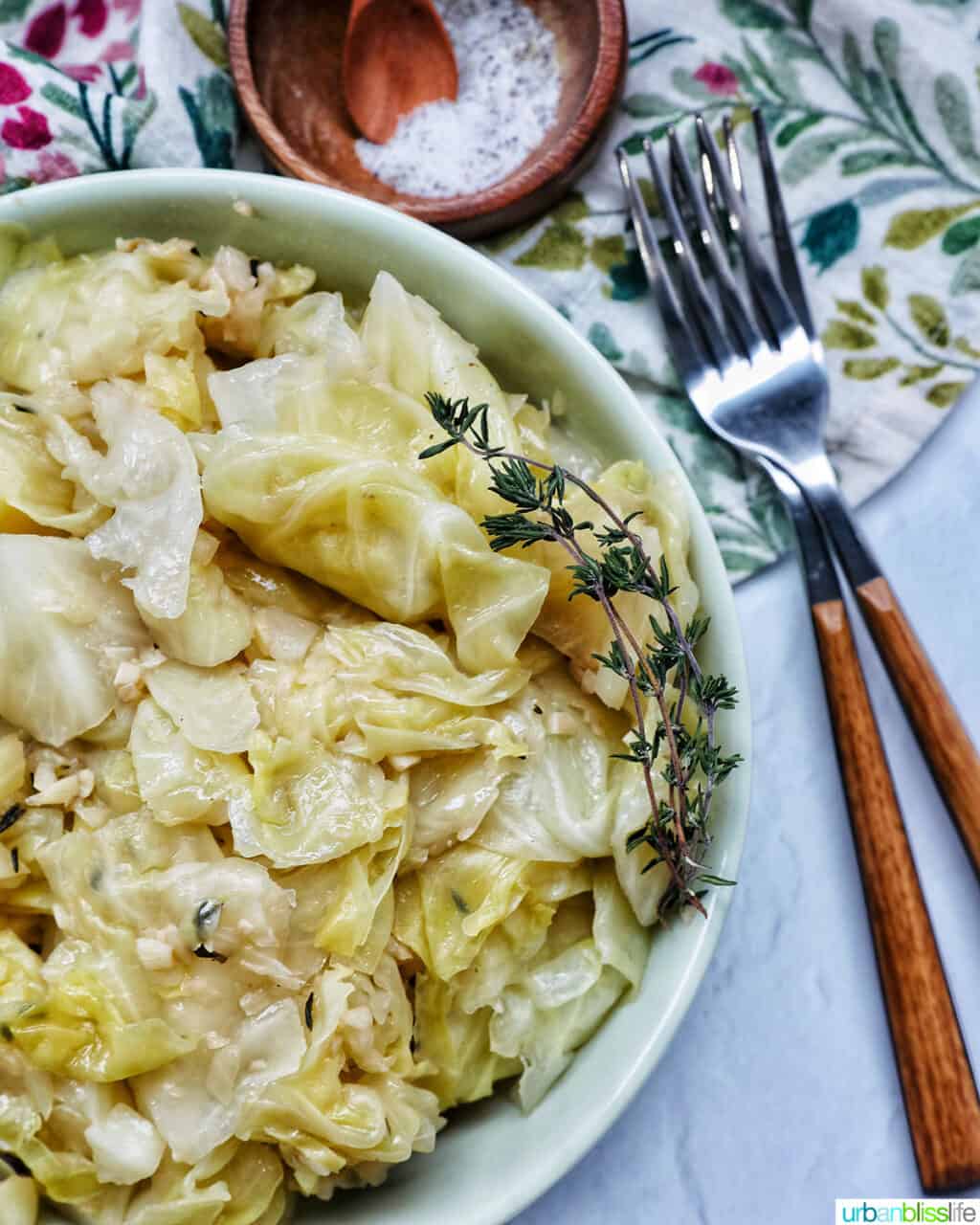 bowl of cooked instant pot cabbage with thyme sprigs, forks, and salt & pepper.