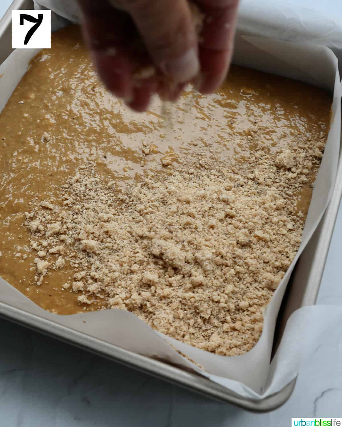 hand spreading streusel topping later on top of wet batter to make Irish coffee cake.