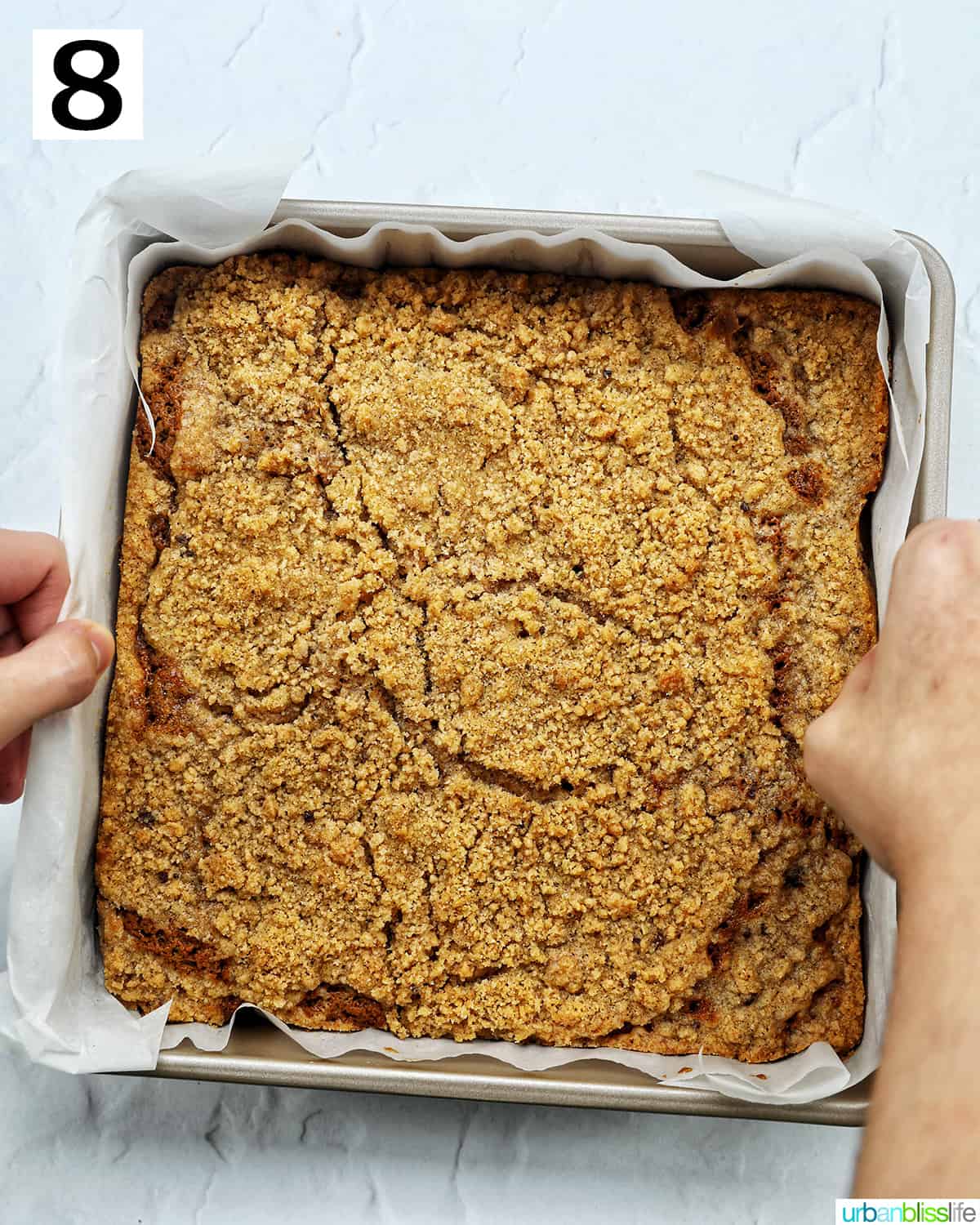 hands lifting Irish coffee cake and parchment paper out of the baking pan.