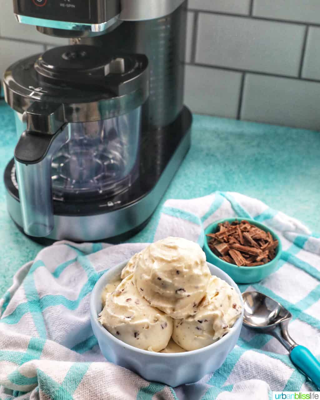 bowl of stracciatella ice cream scoops with bowl of chocolate shavings on the side in front of a Ninja Creami machine.
