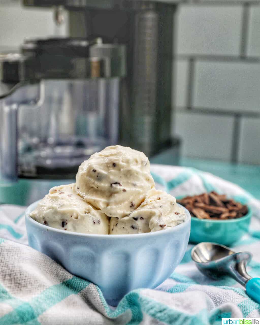 bowl of stracciatella ice cream scoops with bowl of chocolate shavings on the side with a Ninja Creami machine in the back.