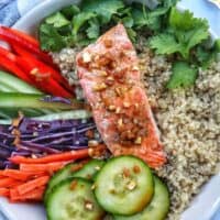 teriyaki salmon on a bed of quinoa with side of sliced colorful vegetables and a fork.