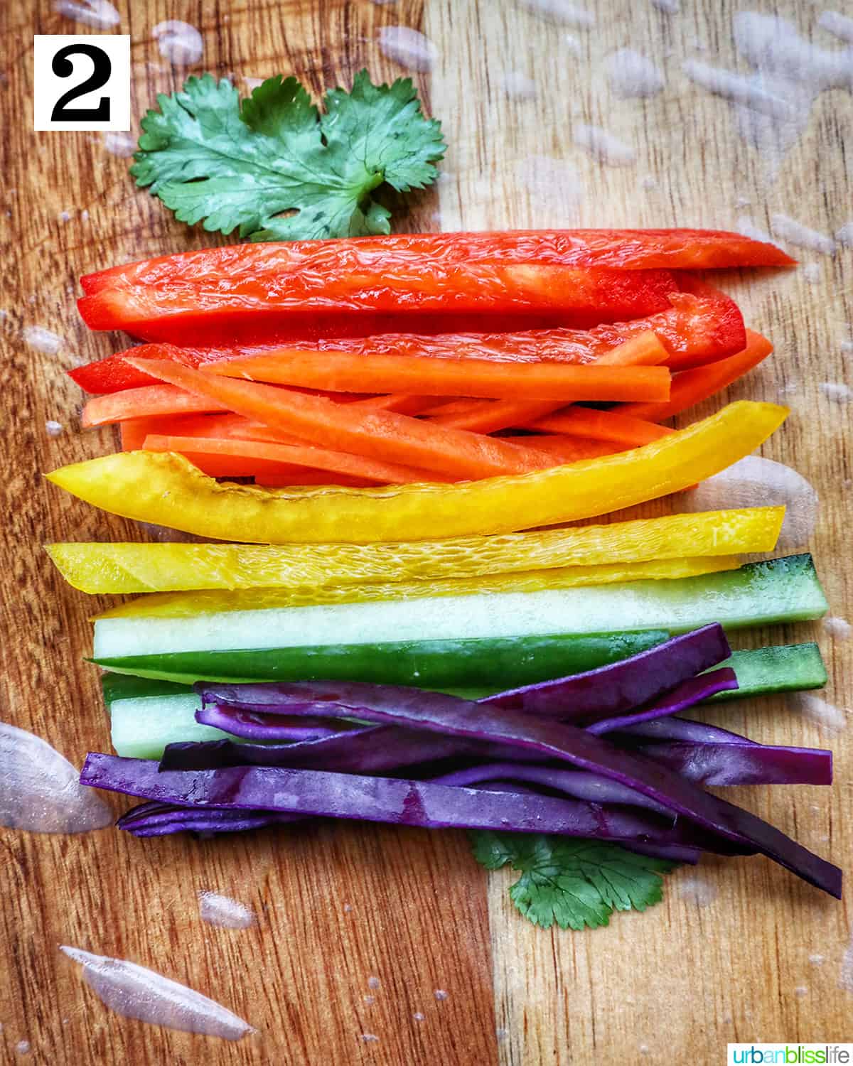 rice paper roll topped with sliced colorful vegetables on a wooden cutting board.