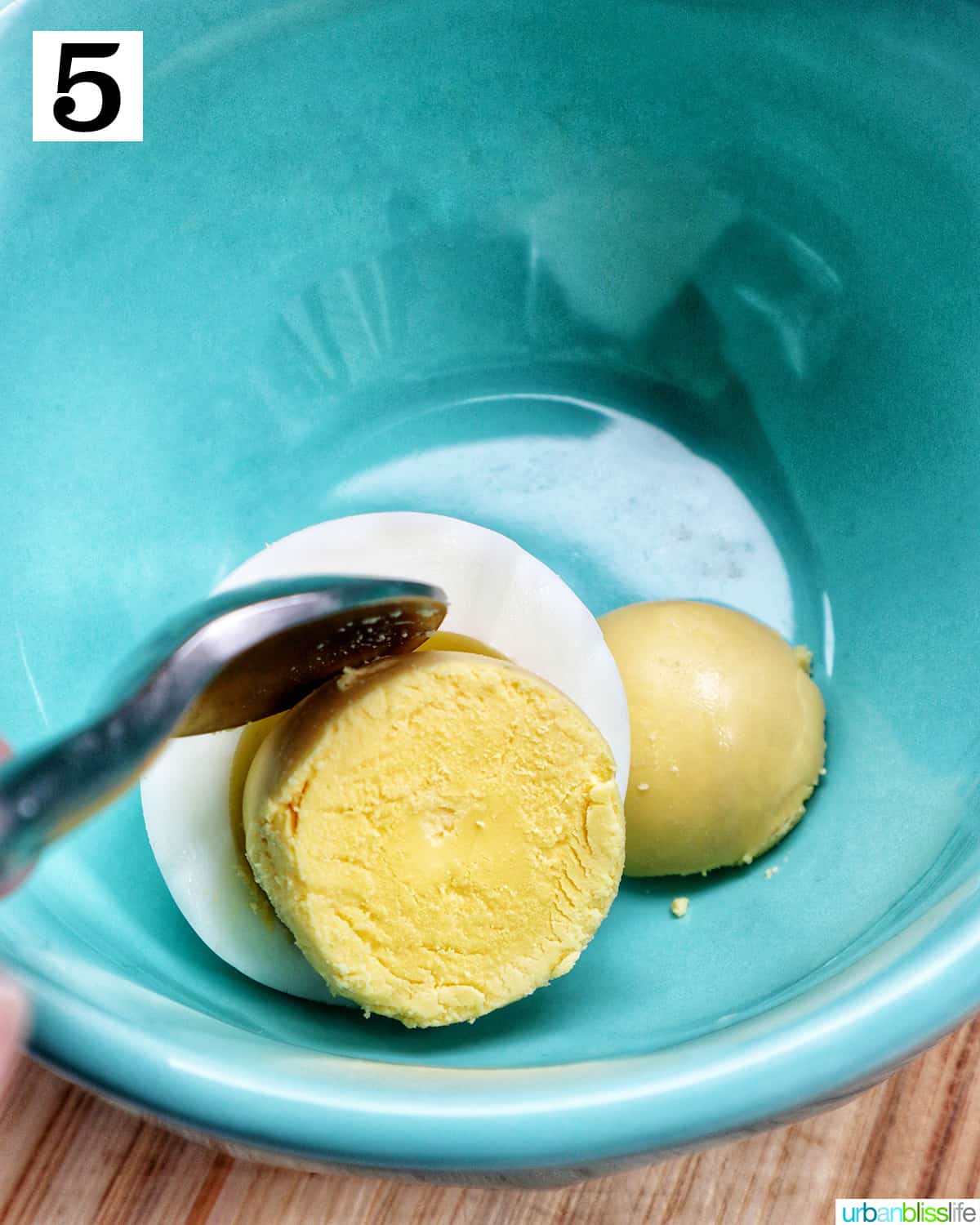 blue bowl with a hardboiled egg and spoon scooping out the egg yolk.