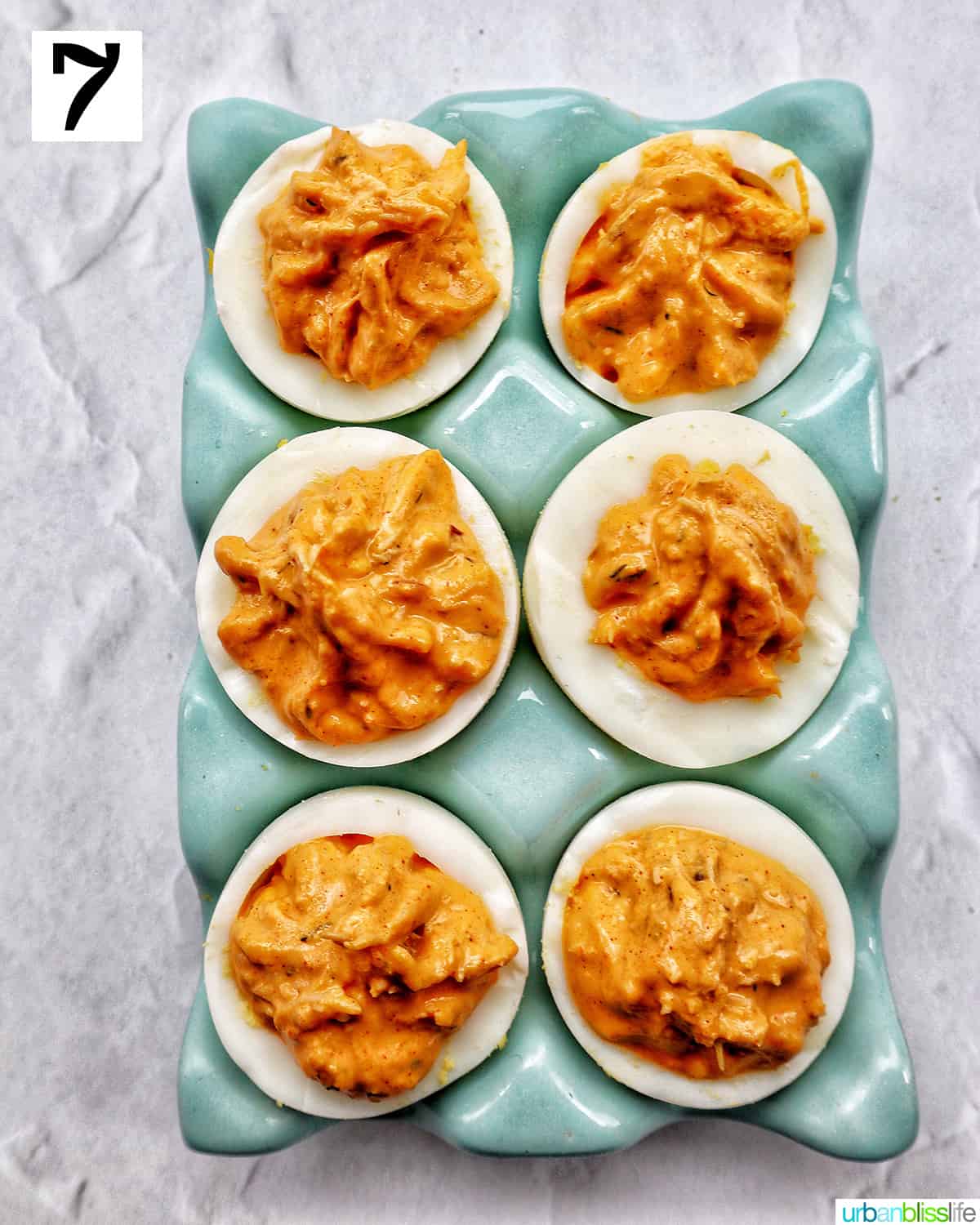 six crab deviled eggs in a blue egg holder.