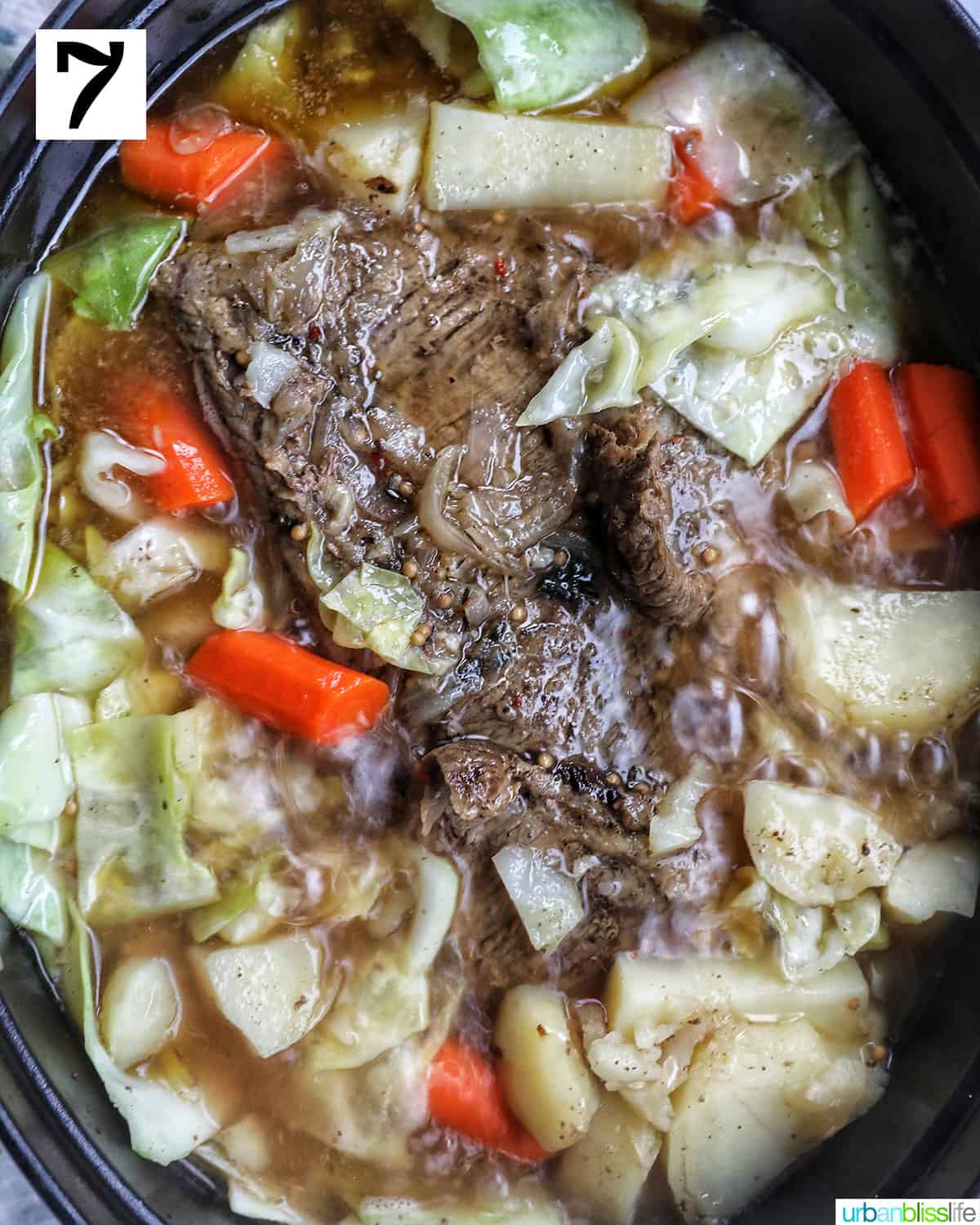brisket in a Dutch oven with carrots, potatoes, and cabbage.