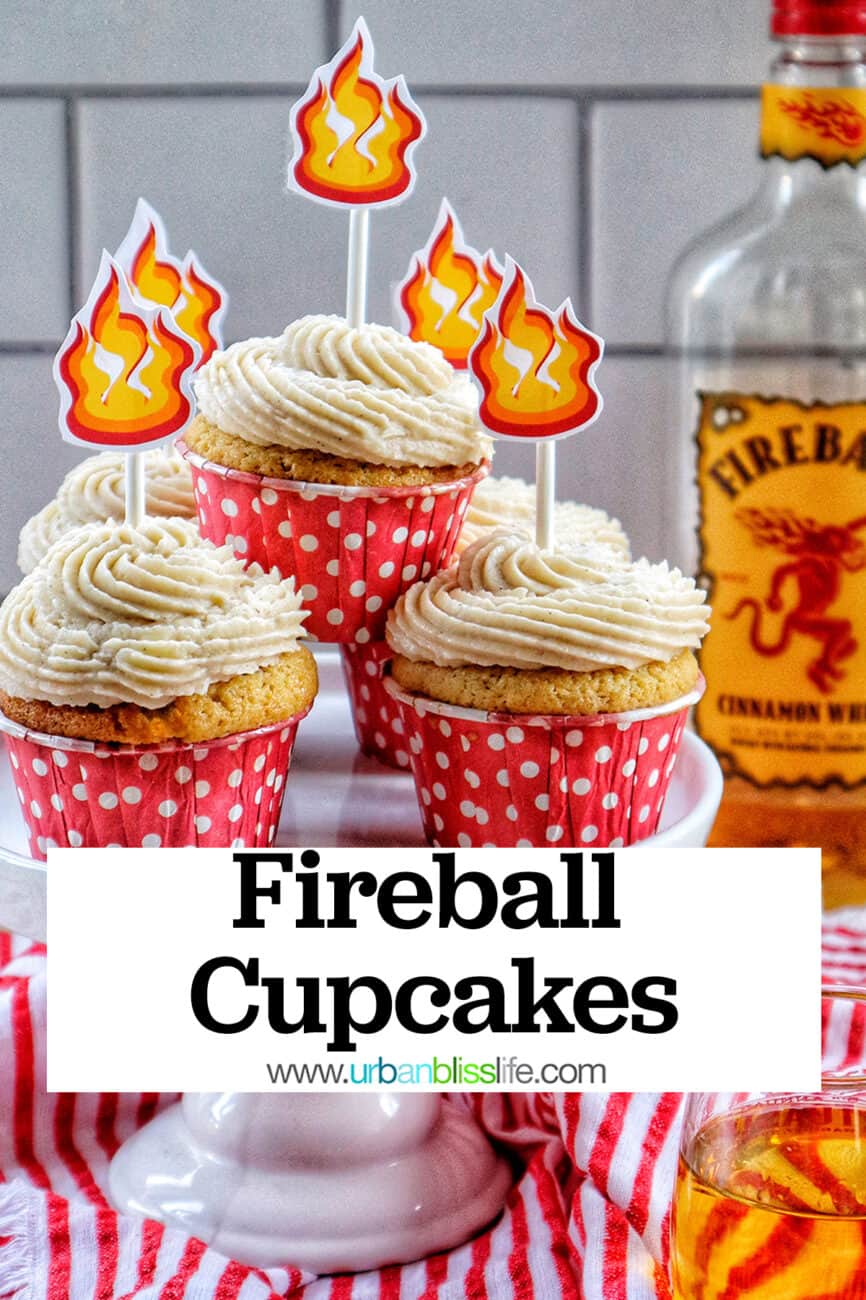 fireball cupcakes in red and white polka dot cupcake liners on a cake pedestal with buttercream frosting and fire sticker decorations on top and a bottle of Fireball in the background.