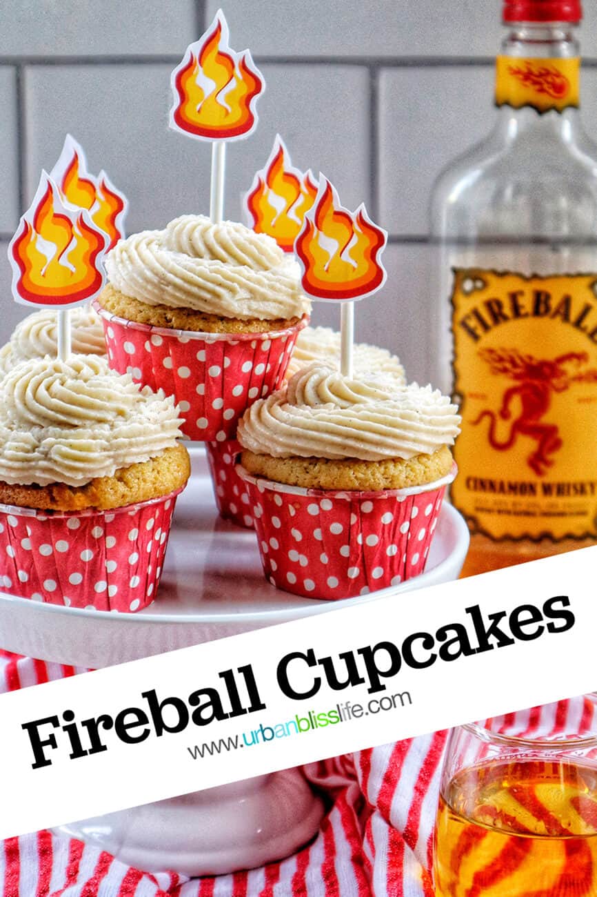fireball cupcakes in red and white polka dot cupcake liners on a cake pedestal with buttercream frosting and fire sticker decorations on top and a bottle of Fireball in the background.