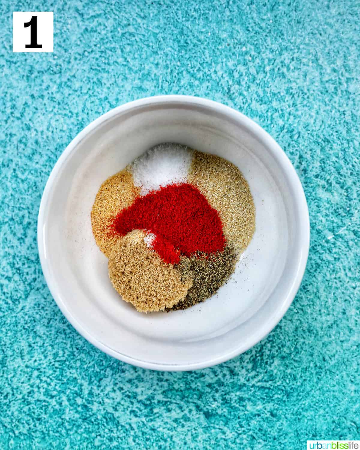 herbs and seasonings in a white bowl on blue background.