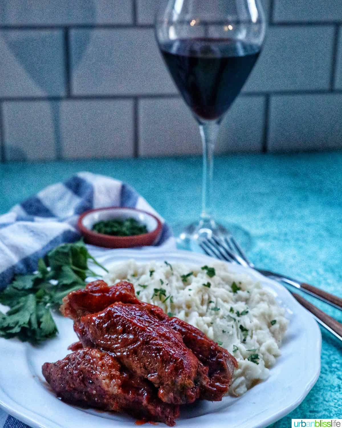 plate of Instant Pot country style ribs and mashed potatoes with herbs and a glass of red wine.