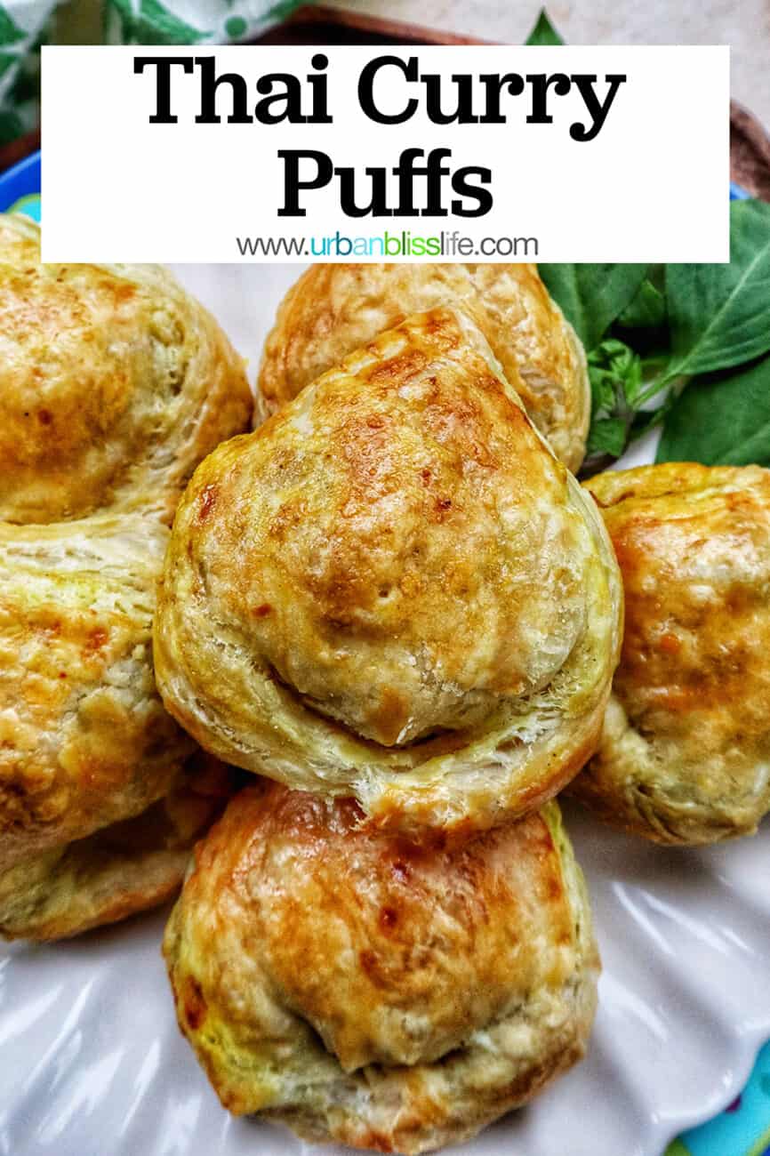 several baked Thai curry puff appetizers on a plate with side of Thai basil with text that reads Thai Curry Puffs.