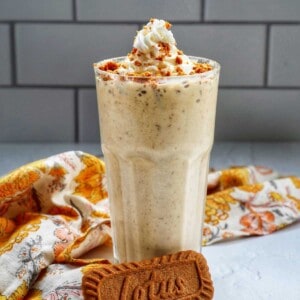 Biscoff Milkshake in a milkshake glass with a yellow floral kitchen linen and biscoff cookie.