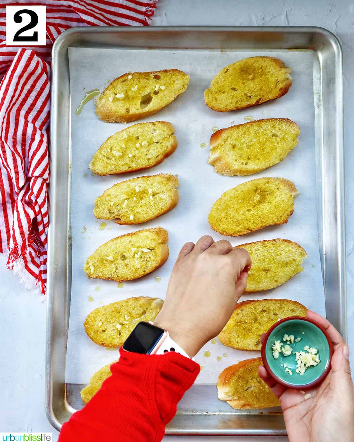 hand sprinkling garlic onto crostini slices on a baking sheet.