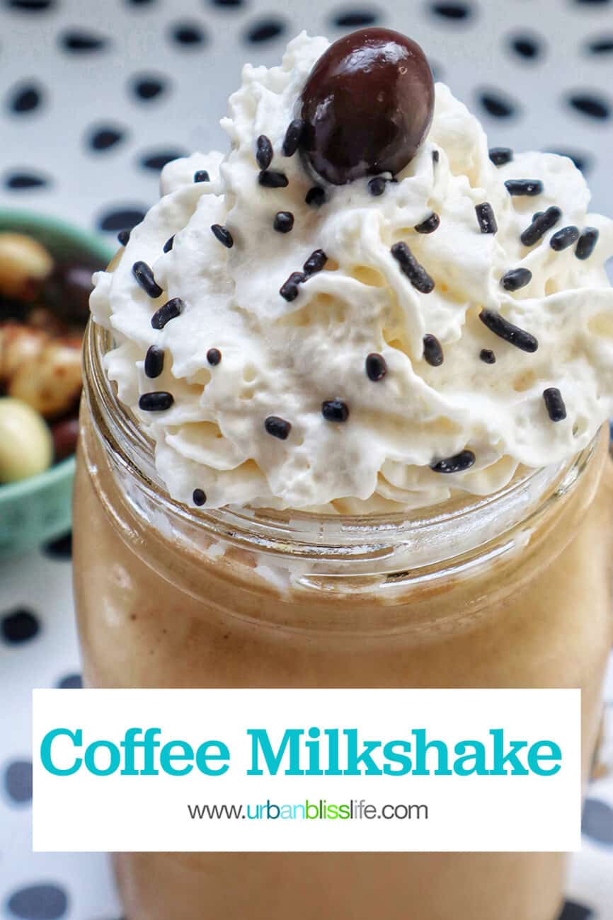coffee milkshake in a mason jar mug with whipped cream and chocolate covered espresso beans on a polka dot table.