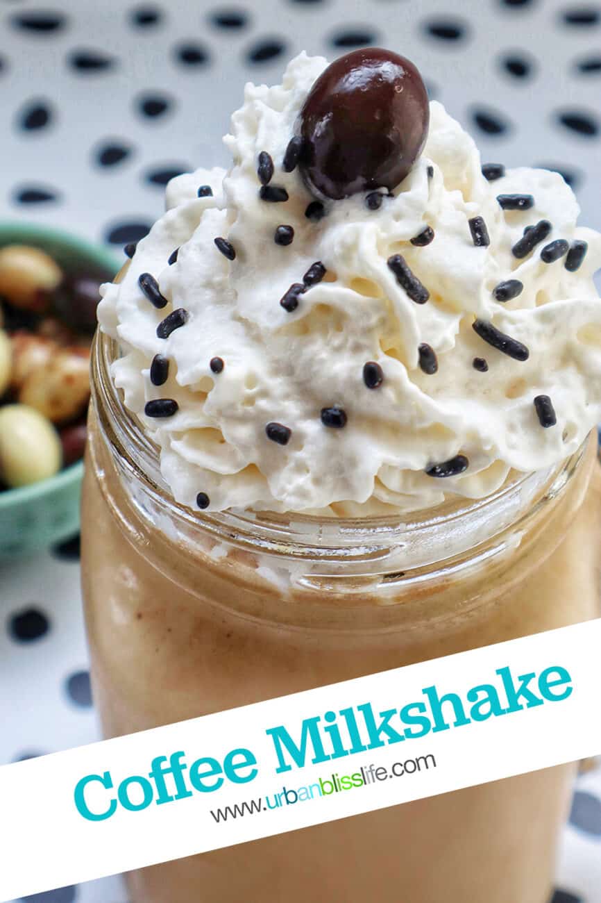 coffee milkshake in a mason jar mug with whipped cream and chocolate covered espresso beans on a polka dot table.