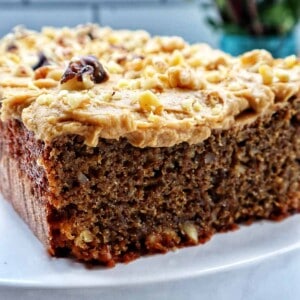 A coffee walnut loaf cake with coffee buttercream frosting on a white pedestal.