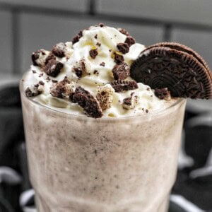 Cookies & Cream Milkshake in a tall glass with whipped cream topping and crushed Oreo cookies on top.
