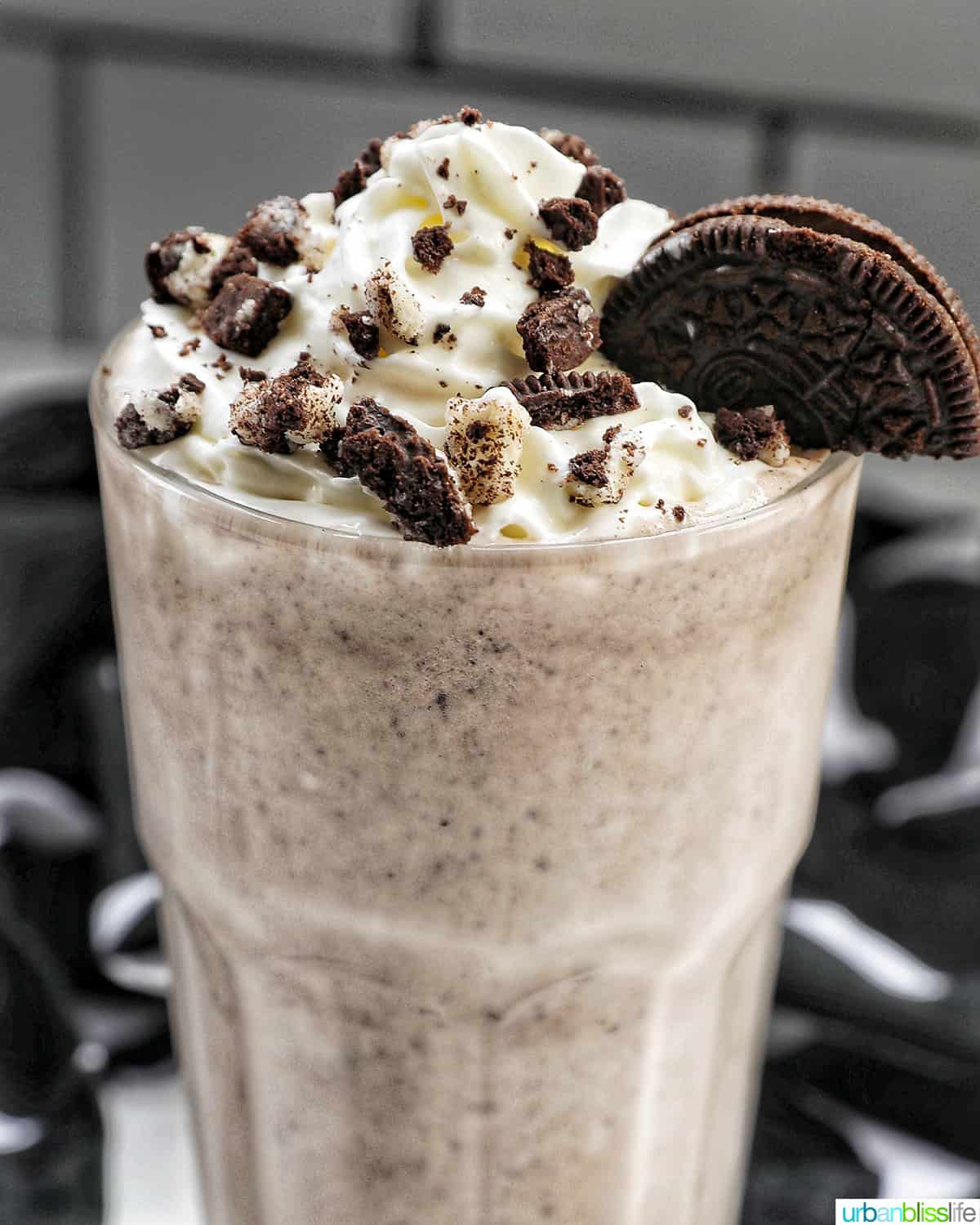 closeup of Cookies & Cream Milkshake in a tall glass with whipped cream topping and crushed Oreo cookies on top.
