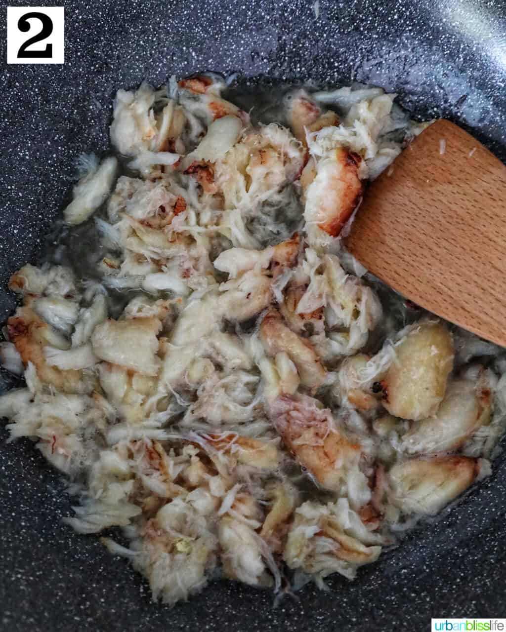 crab meat cooking in a wok with a wooden spoon.