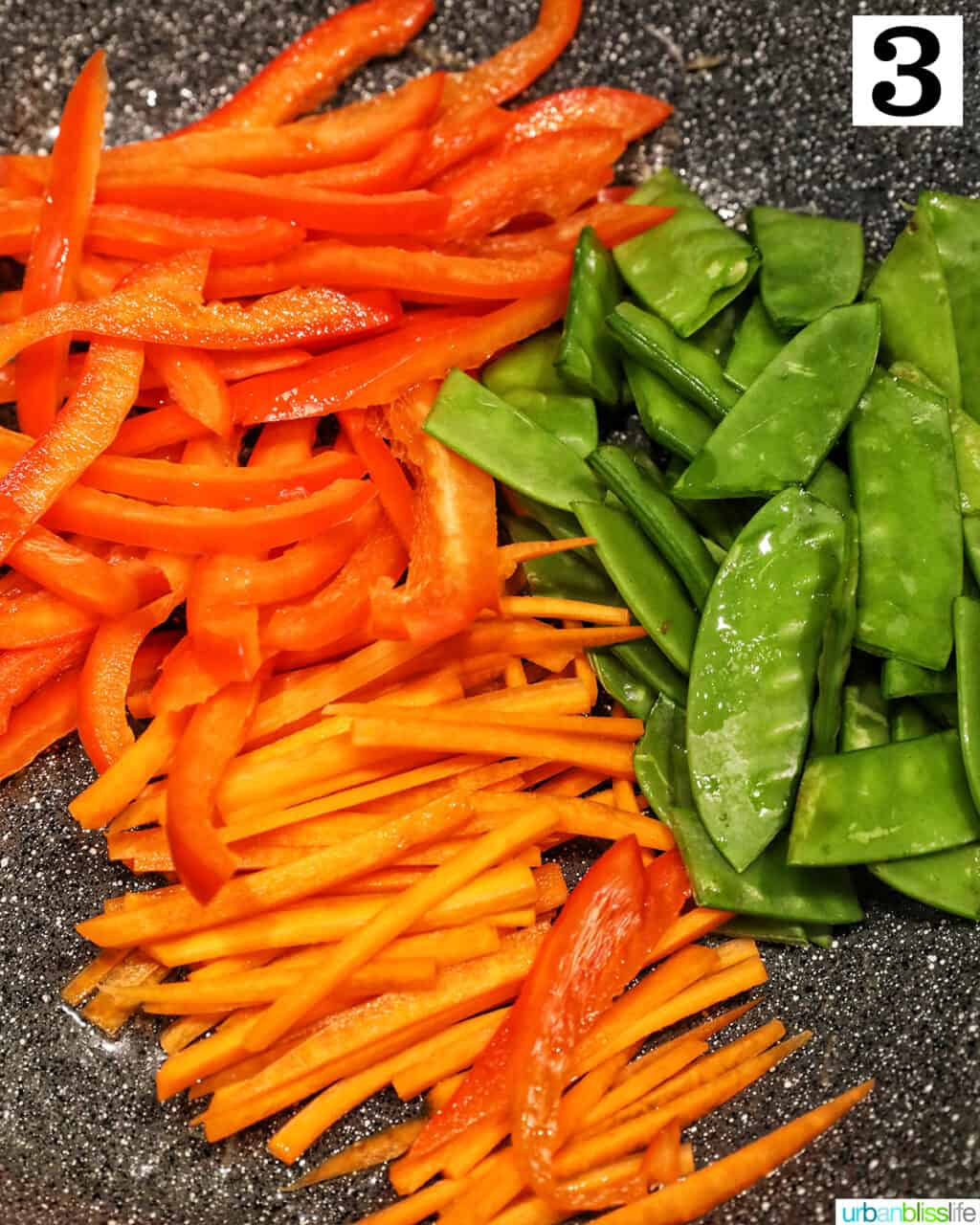 wok with sliced carrots, red bell pepper, and snow peas to make crab pancit filipino noodles.