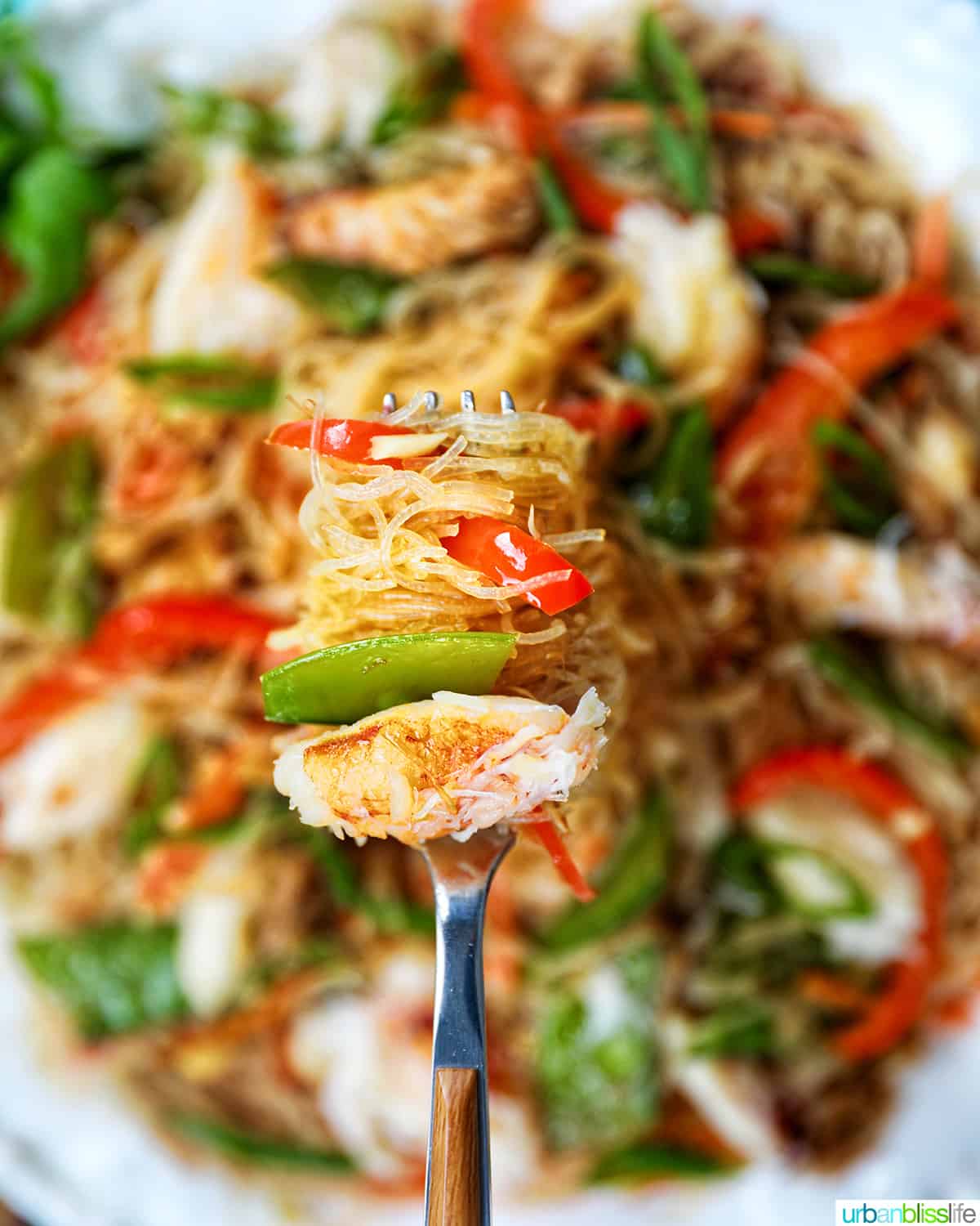 fork full of crab pansit filipino rice noodles lifted above a bowl full of crab pancit.