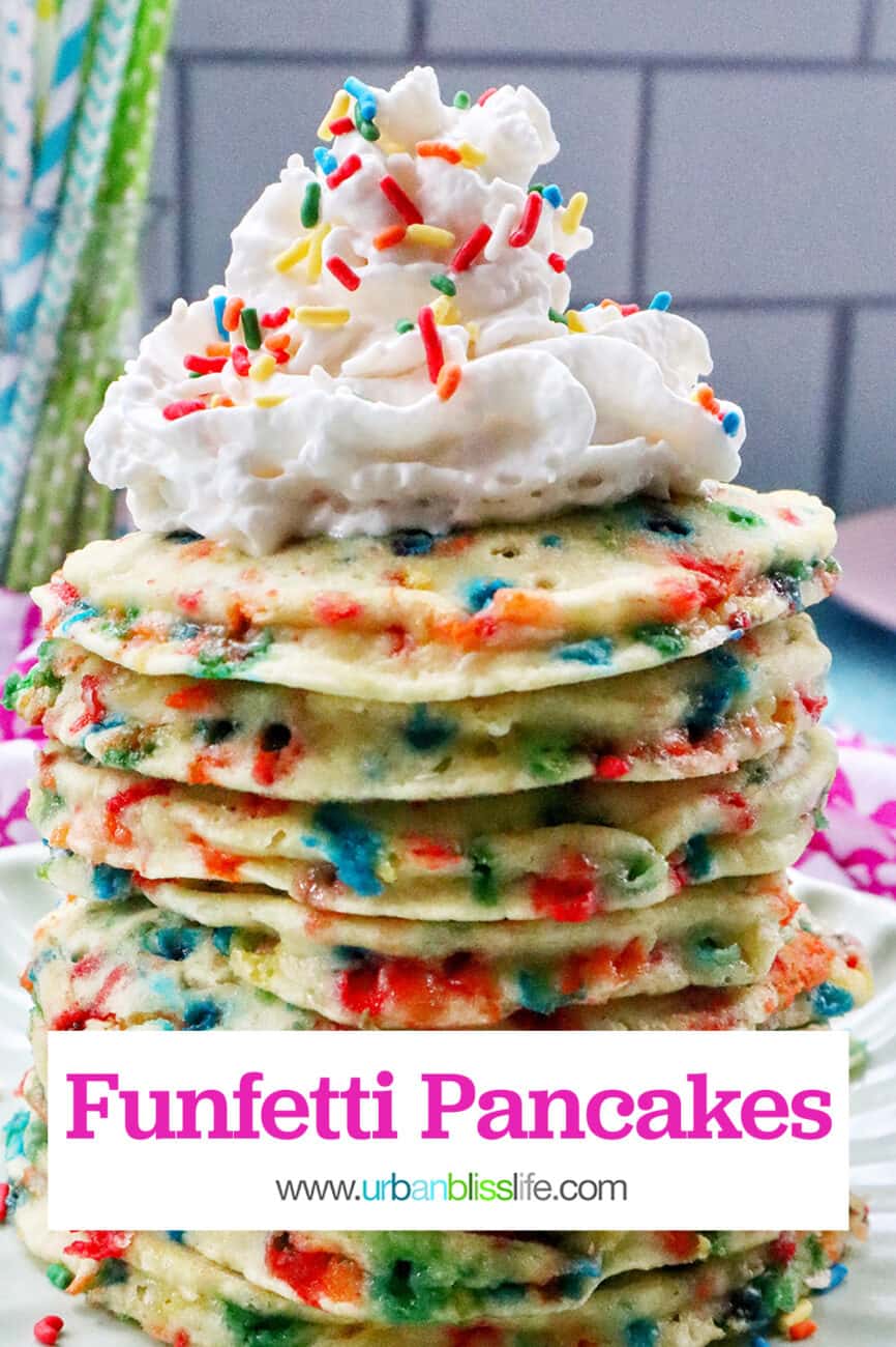 huge stack of funfetti pancakes with whipped cream and sprinkles on a scalloped green plate.